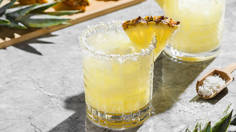A pineapple cocktail, rimmed with dessicated coconut and a pineapple wedge.