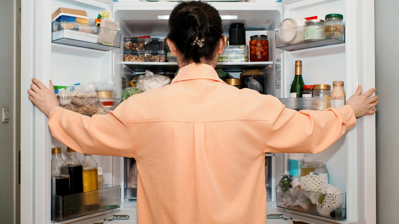 A person stands in front of an open refrigerator.