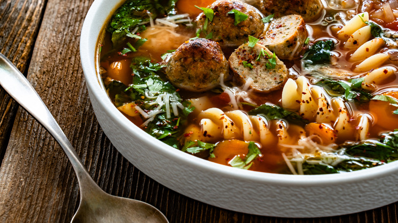A spoon sits beside a white bowl filled with Italian soup