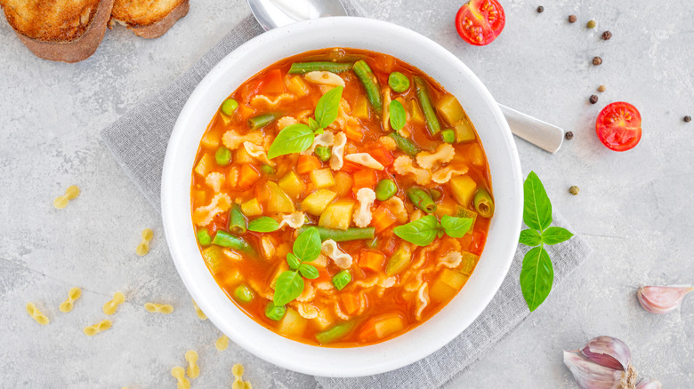 A white bowl is filled with minestrone soup