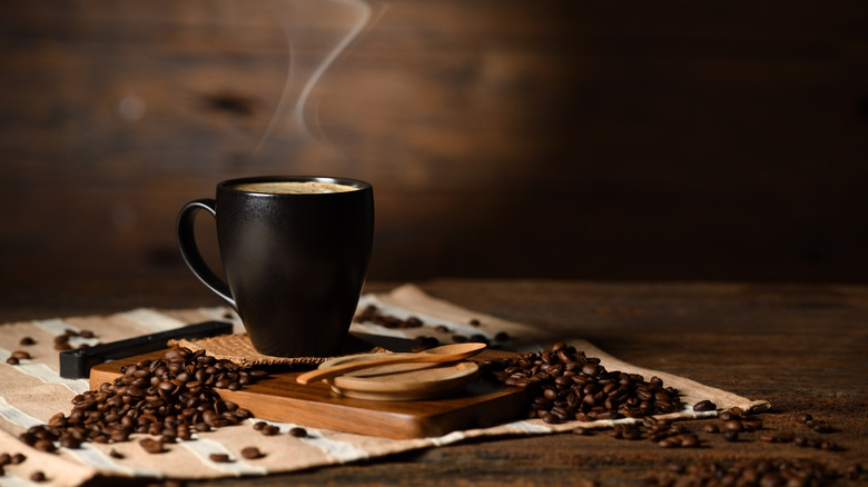 Black cup of coffee with beans on wood