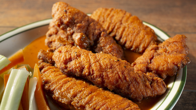 A plate of chicken tenders next to celery and carrot