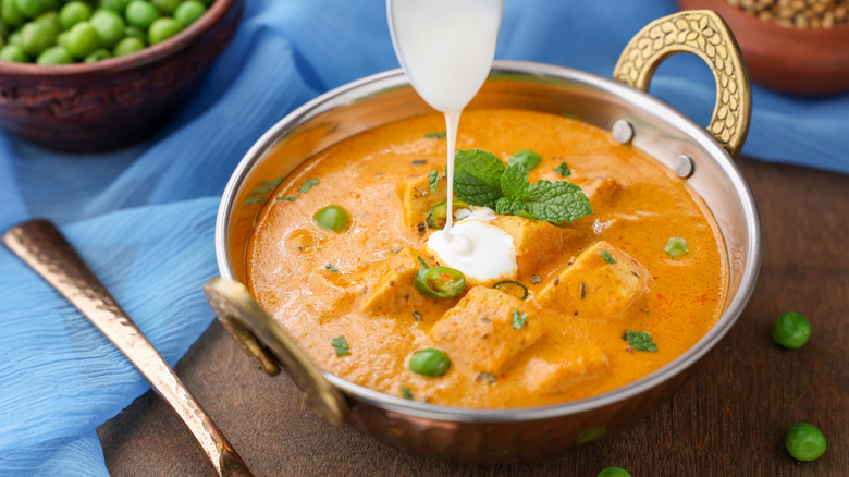 Pouring a spoonful of heavy cream on matar paneer curry