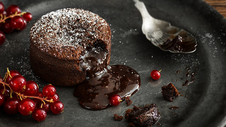 Molten chocolate lava cake dusted in icing sugar on black plate with red currants