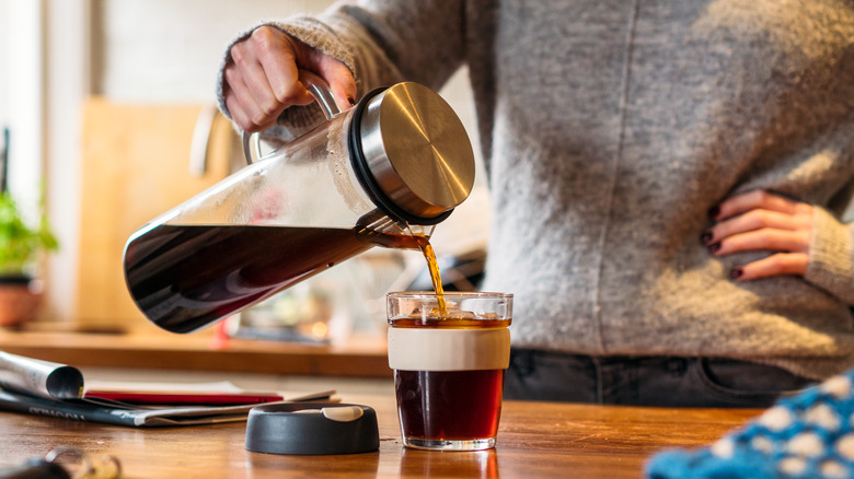 woman pouring cold brew coffee into travel cup