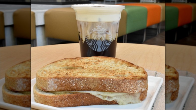 A Starbucks grilled cheese sandwich sits on a plate next to a cup of cold brew with cold foam