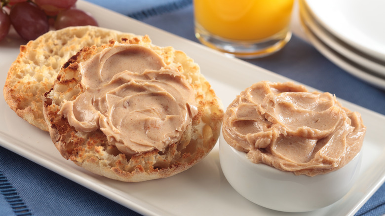 A sliced and toasted English muffin slathered with maple butter sits next to a small ramekin of maple butter