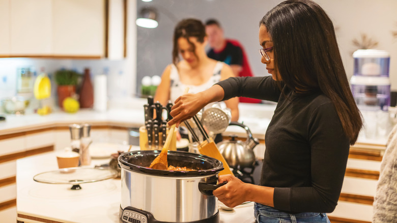 person stirring food in a slow cooker