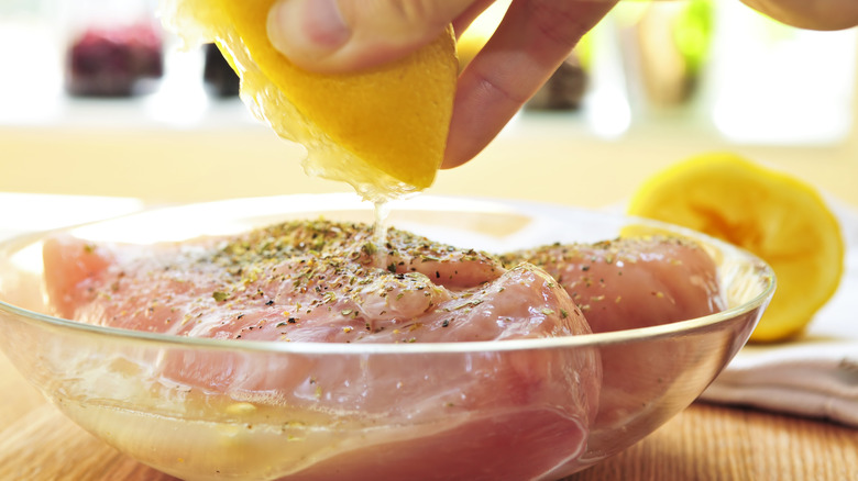 hands squeezing lemon over raw chicken