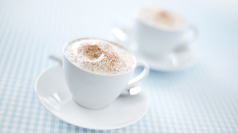 two mugs of steamed milk with cocoa powder