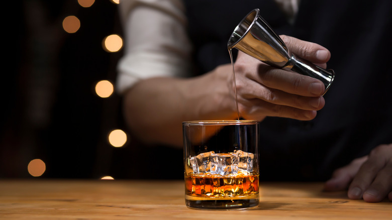 Bartender pouring whisky on wooden bar