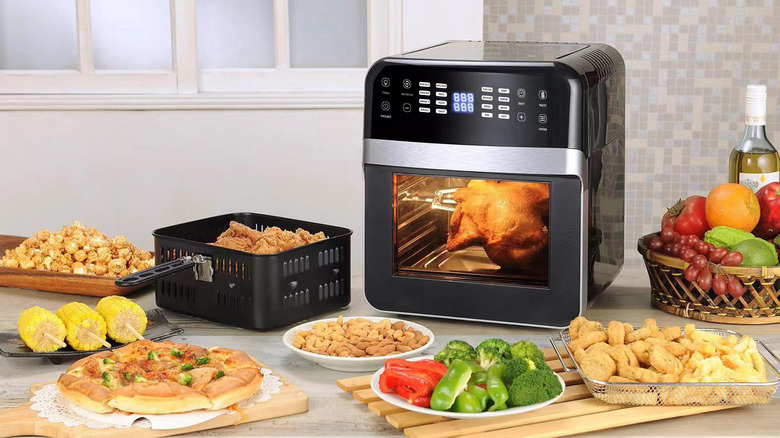 An oven-style air fryer with dishes to be be cooked surrounding it on the counter