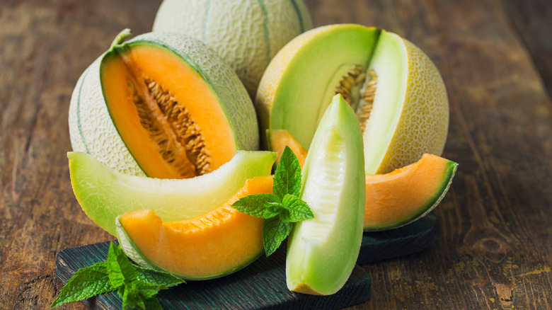 A cantaloupe and honeydew melon sit on a wooden table with pieces cut out and arrayed before them