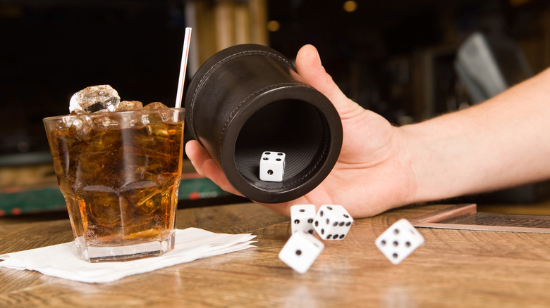 Throwing dice on a table with a drink