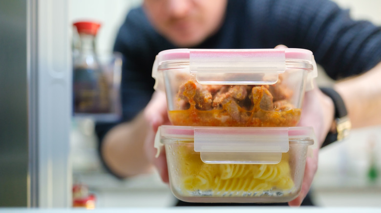 Person placing cooked chicken and pasta in glass containers into the fridge.