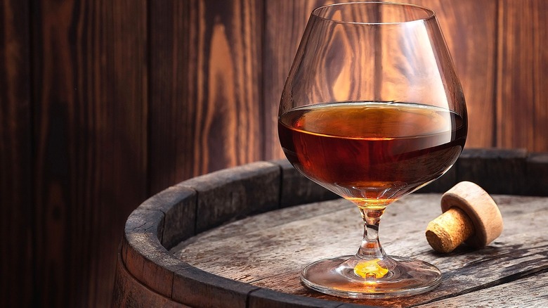 Glass of cognac on an oak barrel with a loose cork