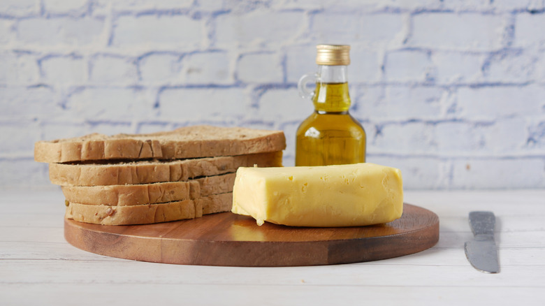 A block of butter and a jar of oil sit next to some bread slices