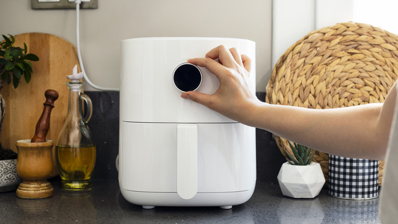 A hand adjusts the knob on an air fryer.
