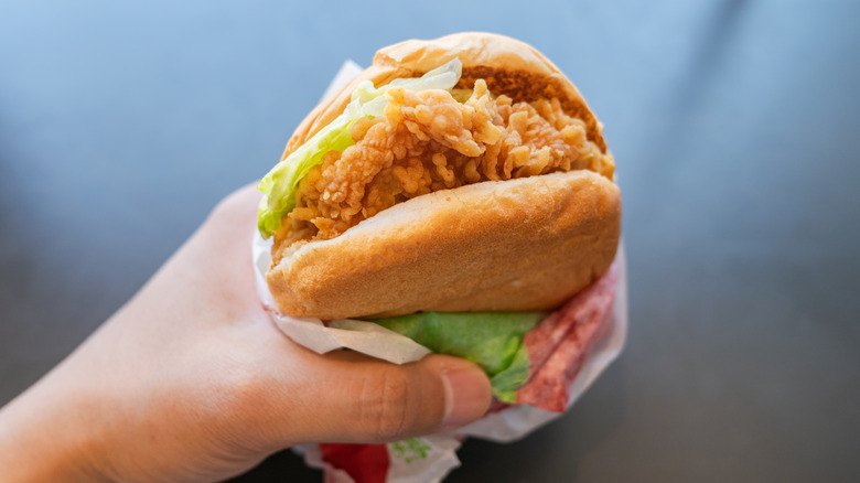 A hand holds a chicken sandwich in its wrapper.