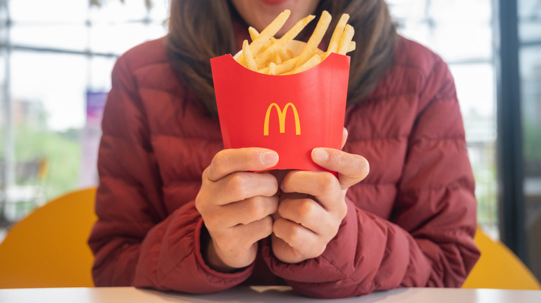 A person in a red jacket holding a box of McDonald's fries