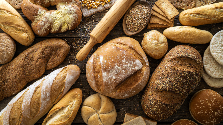 A table full of artisan bread, a rolling pin, and raw grains.