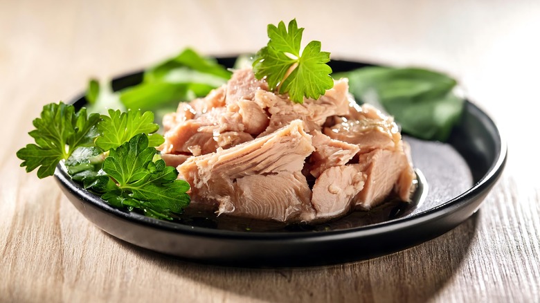 Canned tuna on a black plate with fresh herbs