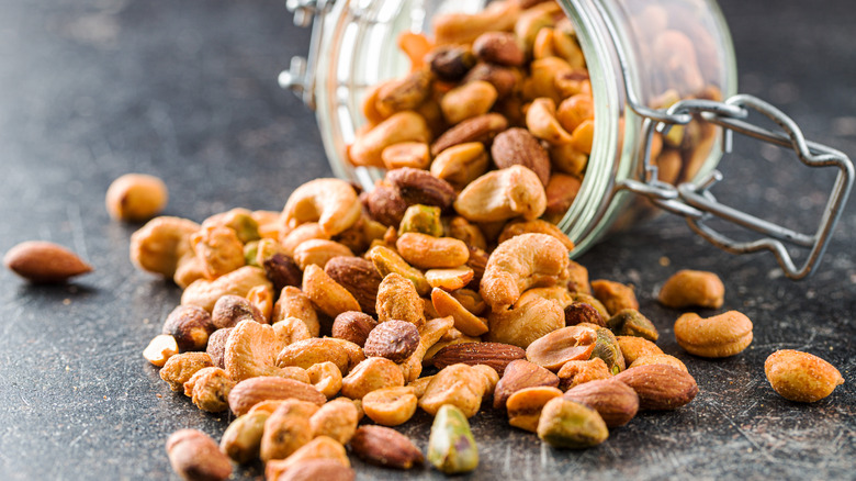 A mixture of roasted nuts spills out of a glass jar laying on its side