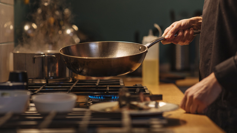 hands holding wok over stovetop burner