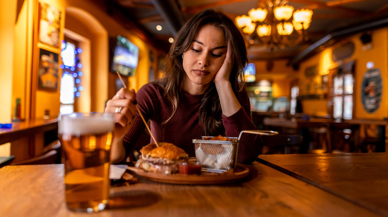 A diner picks at their burger unhappily inside a restaurant