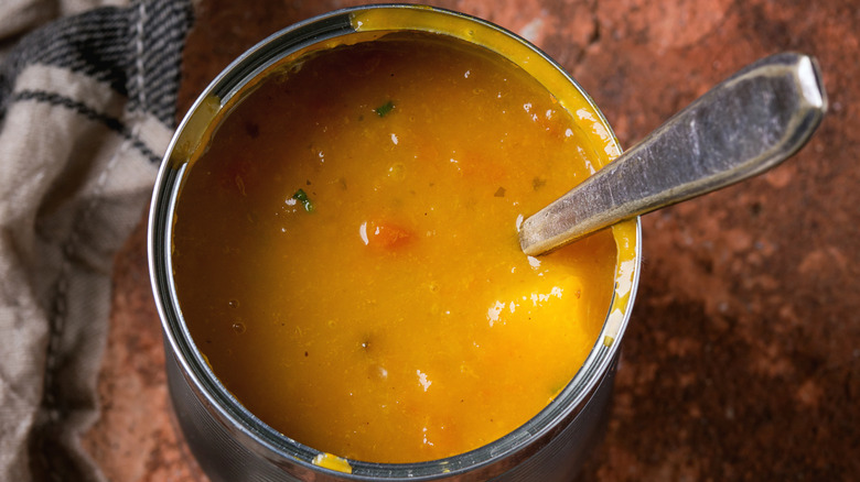 Opened tin of vegetable soup with a spoon in it.