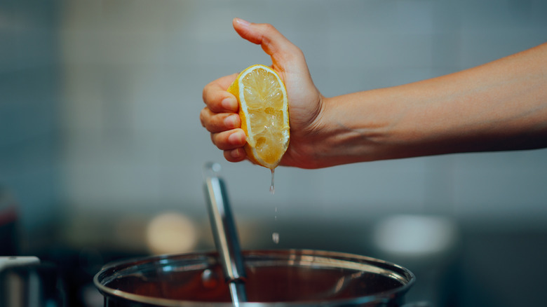 A cook squeezes lemon into a pot of soup.