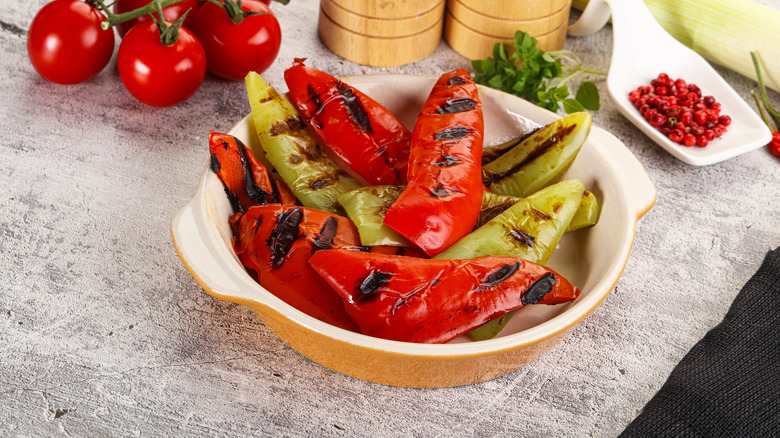 Big pieces of grilled bell pepper sit in a casserole dish surrounded by peppers and tomatoes
