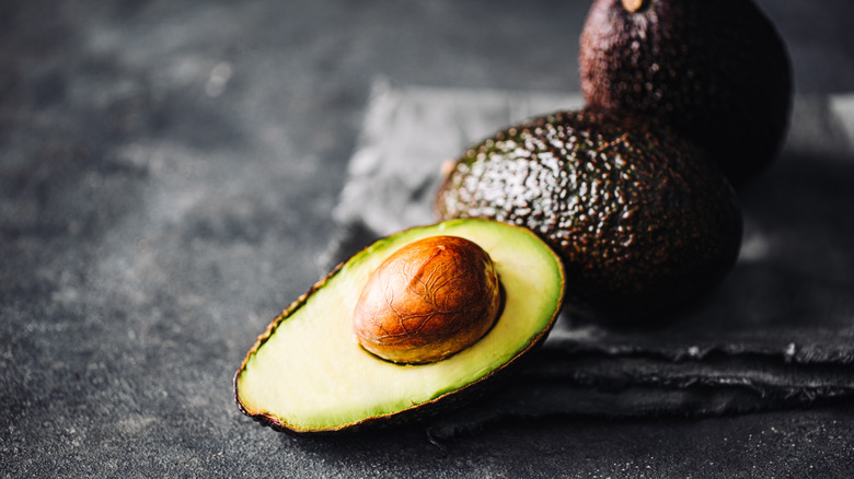 Whole avocados next to a sliced one