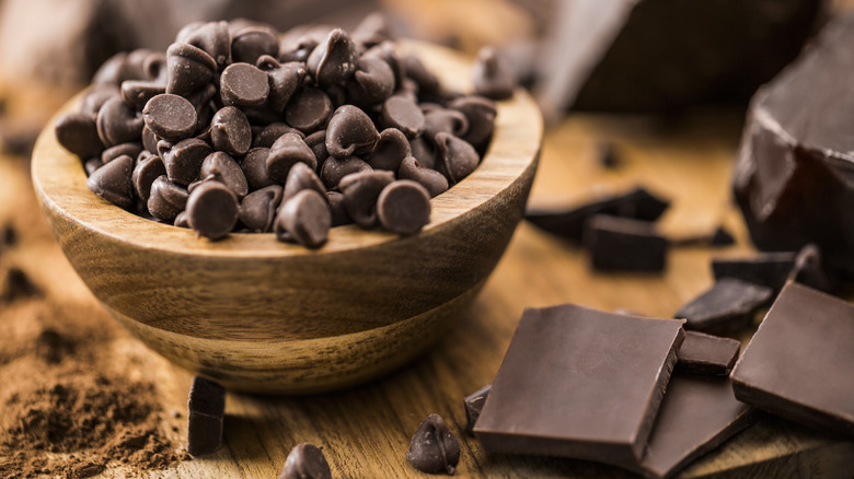 A bowl of chocolate chips next to chocolate pieces