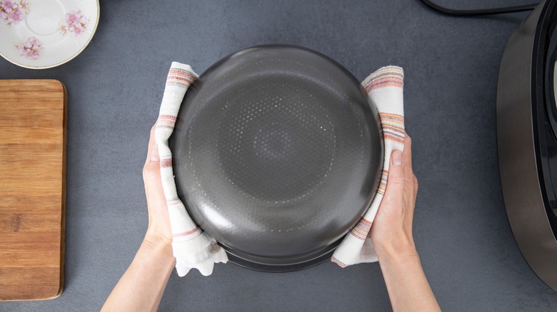 Hands hold an inverted cake pan using dish towels for protection