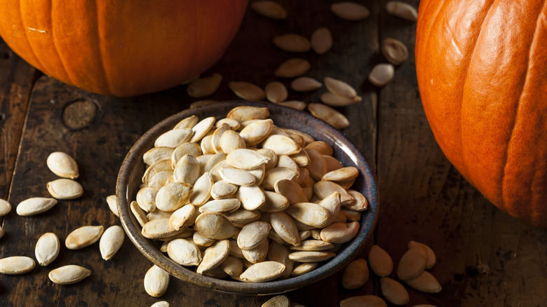 bowl of pumpkin seeds next to pumpkins