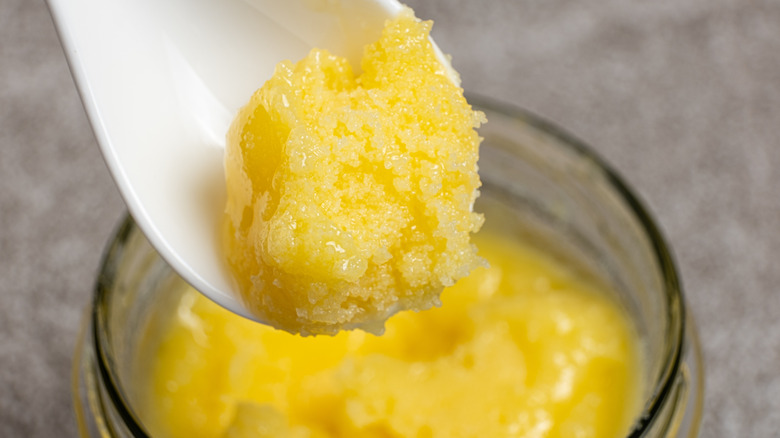 A white spoon holds a spoonful of clarified butter over a clear jar