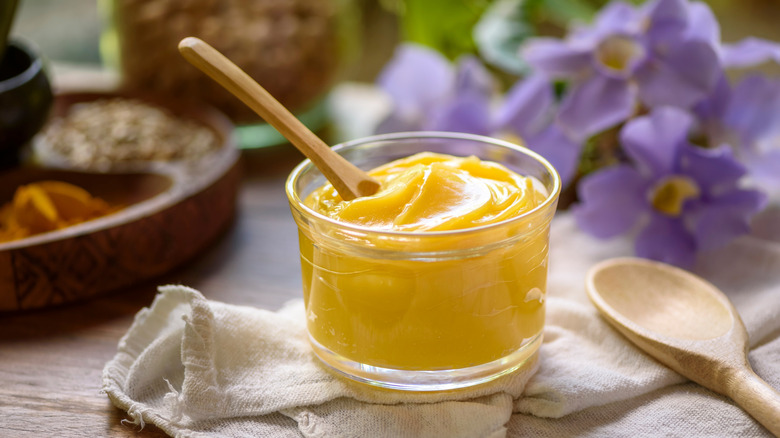 A small glass jar of ghee with a wooden spoon on a decorated table