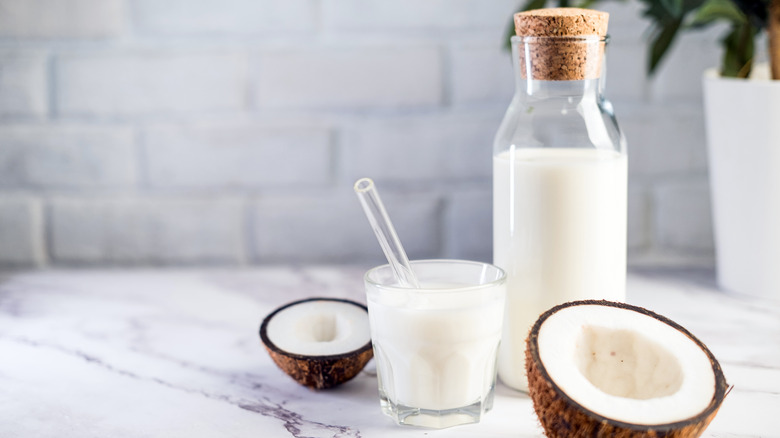 Glass bottle of coconut milk next to halved fruits