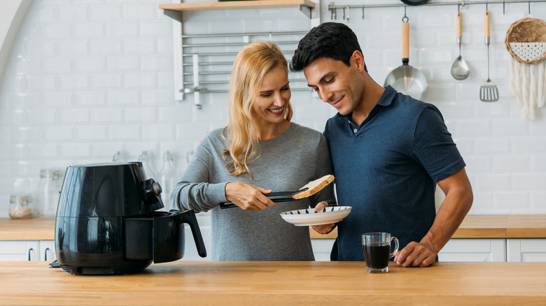 A man and woman serve themselves from an air fryer.
