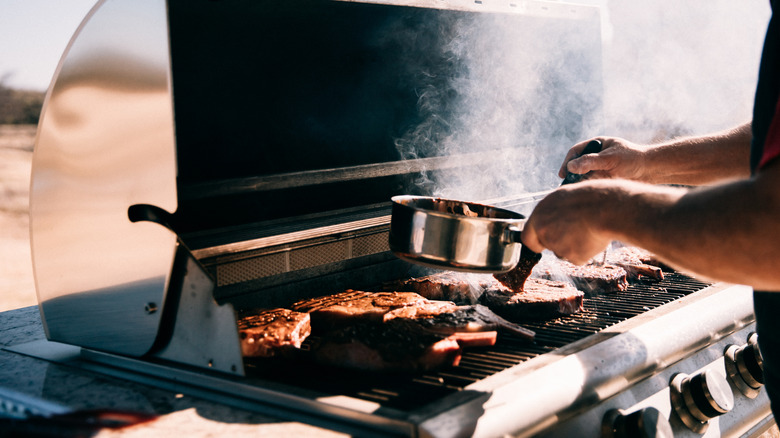 Someone cooks steaks on a gas grill