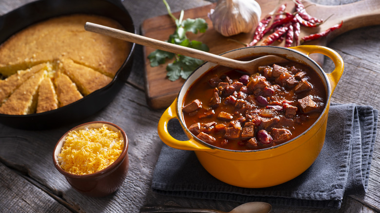 Pot of chili next to cornbread, rice, and aromatics
