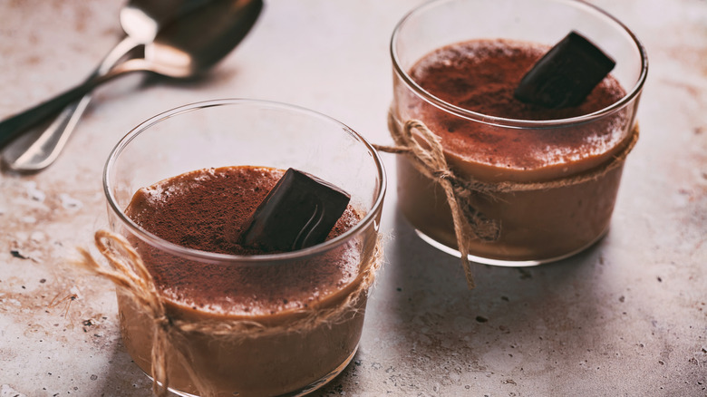 Two chocolate puddings with a chunk of dark chocolate in the glass cups