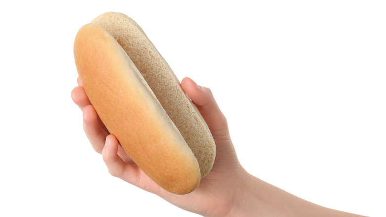 hand holding a hotdog bun on a white background