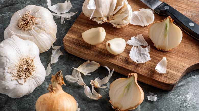 Garlic and onions on a cutting board with peels