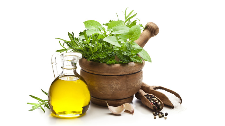 A pot of herbs next to a pitcher of oil, garlic, and peppercorns