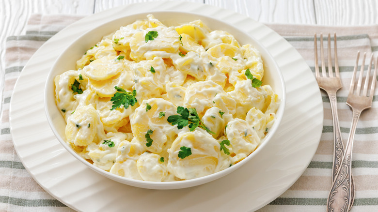 A creamy potato salad sits in a white bowl.