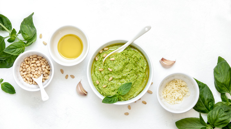 Homemade pesto sits in a bowl, surrounded by its ingredients