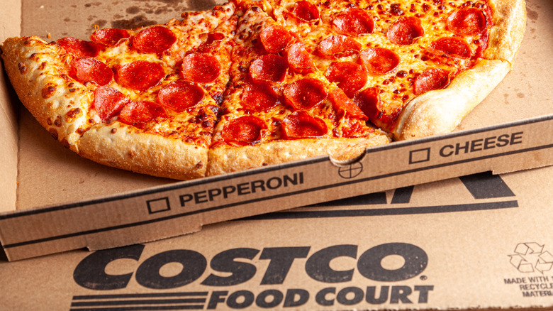 A menu board at a Costco shows images and prices for hot dogs, pizza, and chicken bakes