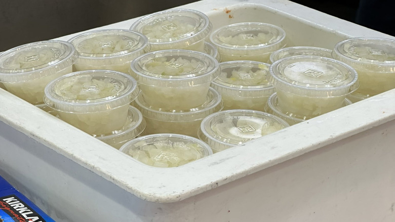Chopped onions inside condiment containers sit in a plastic tub